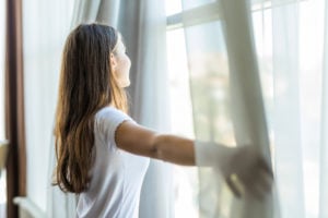 A woman opens curtains in a bedroom