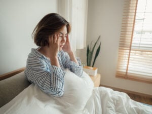 Young woman in bed holding her head to her temples in exhaustion