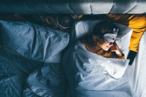 Woman wearing yellow pajamas and sleeping in bed with an eye mask on.